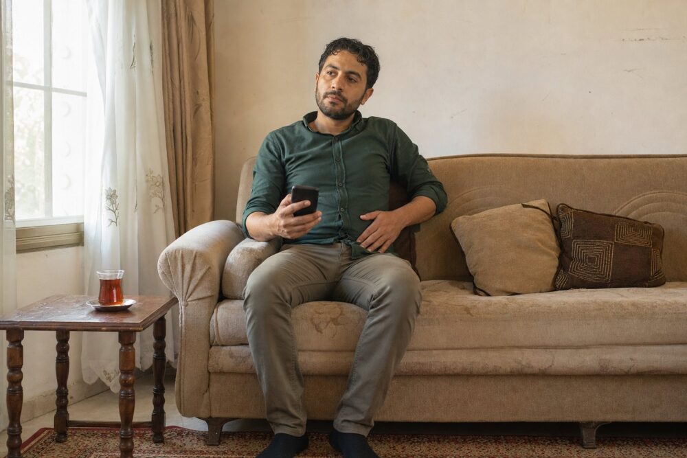 رجل جالس على أريكة في غرفة معيشة يفكّر وهاتفه في يده